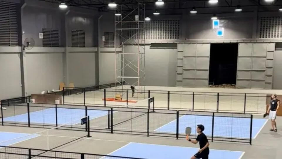 Side-out Pickleball Center — Elevated interior view of Side-out Pickleball Center with multiple light-blue and gray courts, black dividers, and players on court.